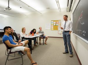 Economics Professor Patrik Hultberg teaches students from a blackboard
