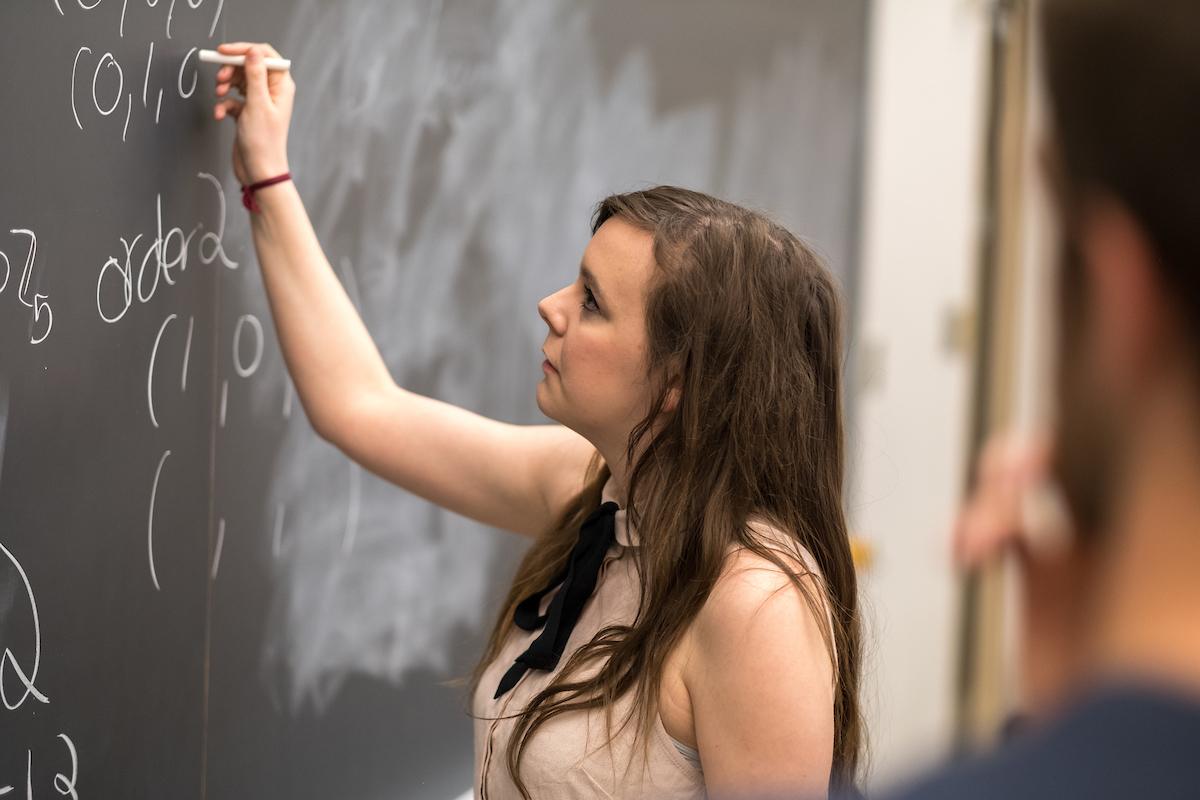 Student writing doing math on a chalk board