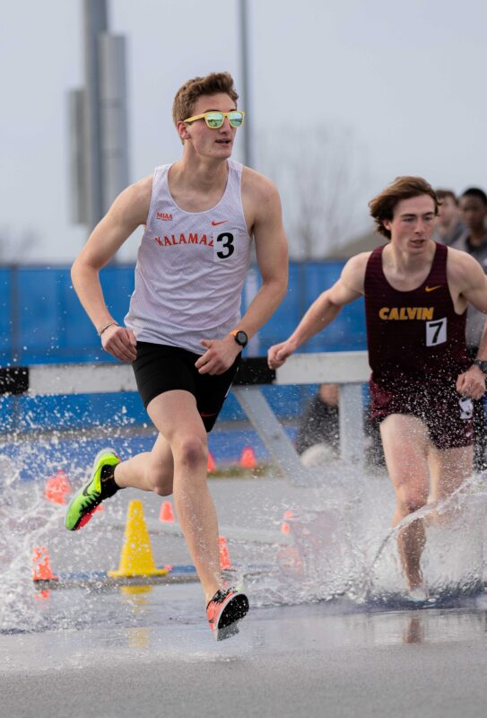 Sam King running in a cross country race with water splashing around his feet.