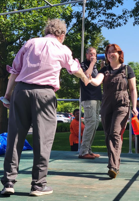 Two male faculty and a female grad-to-be on Commencement stage during rehearsal advice