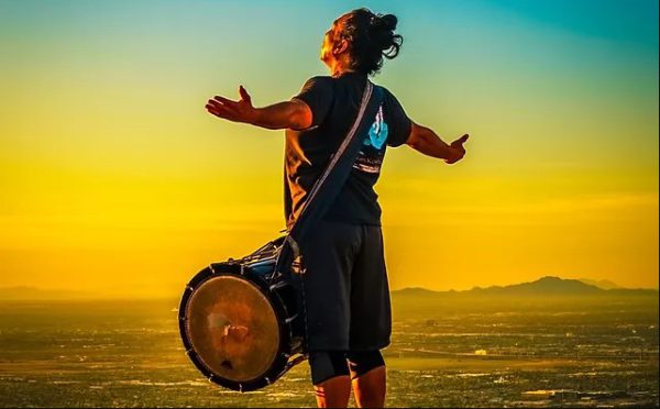 Obon Festival Featured Performer Ken Koshio with stretched out arms and a drum looking over a city.