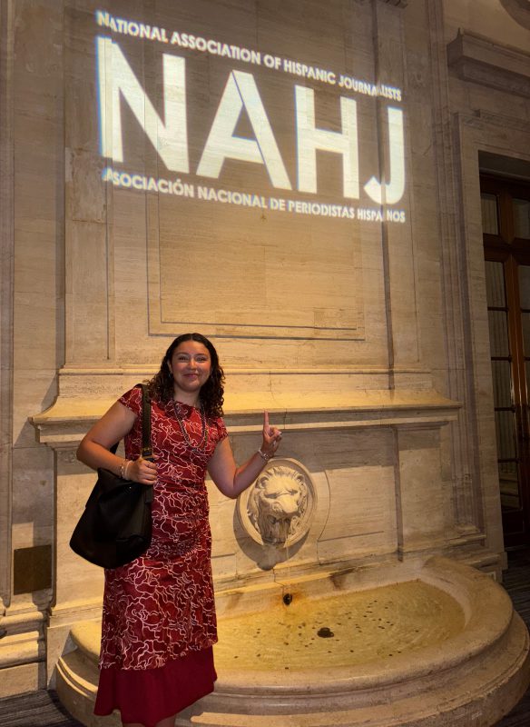New York Times Corps Member Sarah Guerrero Gorostieta stands next to a fountain that has NAHJ projected onto it 