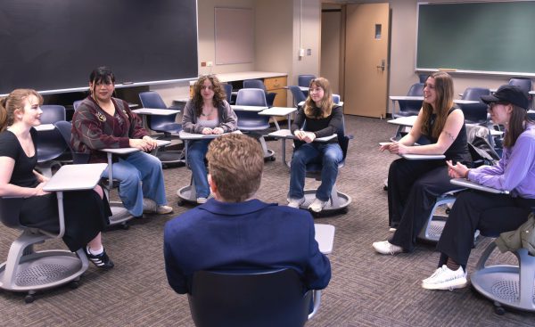 Students in a classroom sit in a semicircle around their professor