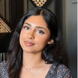 Hibah Khan, a woman with long dark hair, wearing a patterned top and delicate necklace against an indoor background.