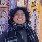Ash Rodriguez, a smiling person with curly dark hair wearing a plaid scarf, set against a colorful, intricately decorated background.