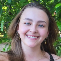 Aubrey Benson, a smiling young woman with long light brown hair and blue eyes, set against a leafy green background.