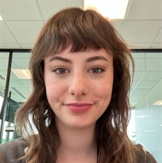 Estelle Metz, a smiling woman with wavy brown hair and short bangs, set against an indoor office setting background.