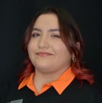McKenna Acevedo, a smiling person with reddish-brown shoulder-length hair, wearing an orange collared shirt under a black top against a solid dark background.