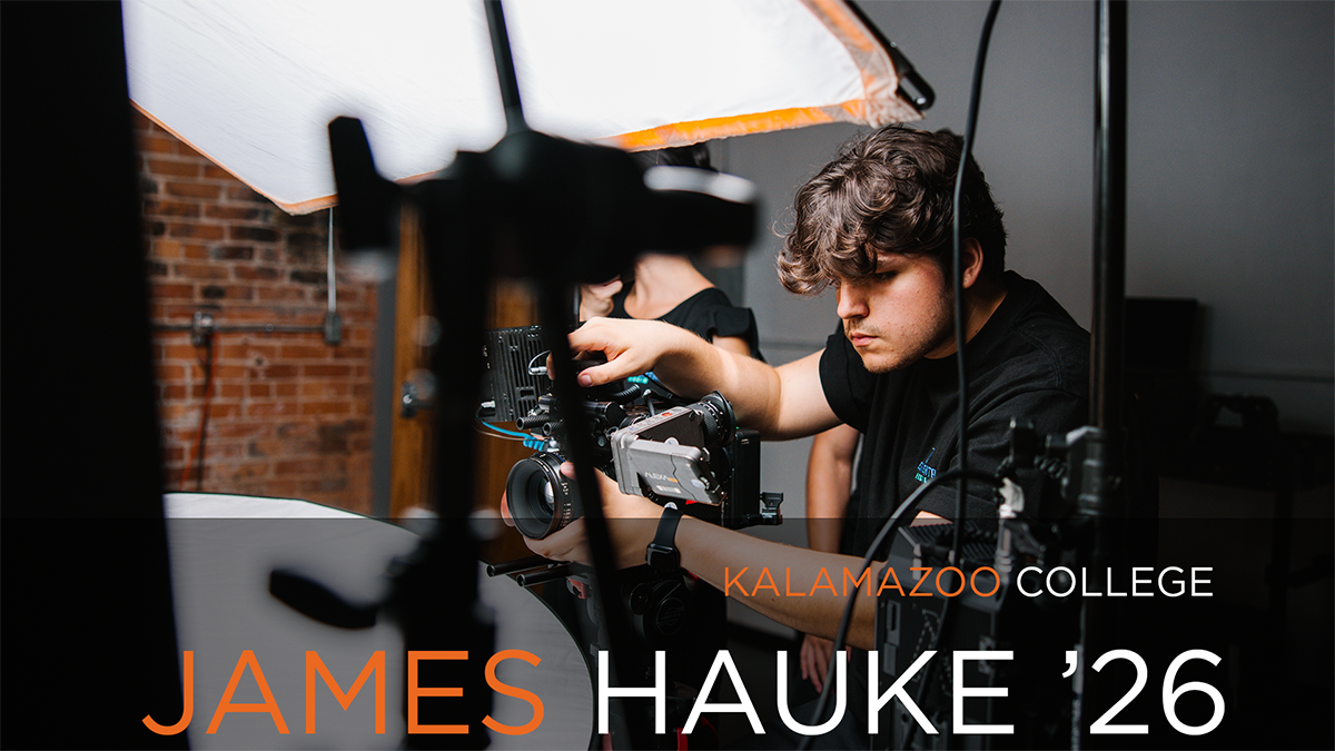 A photo of James Hauke '26 working with a camera setup at his internship. He is wearing a black shirt and adjusting the equipment, with a softbox light and brick wall in the background. The text "KALAMAZOO COLLEGE" and "JAMES HAUKE '26" is overlaid in orange and white.