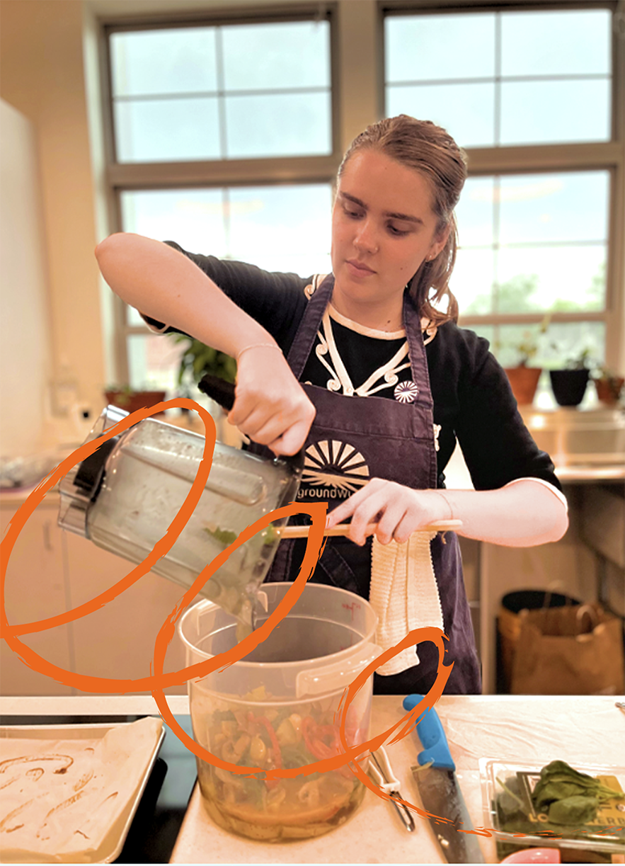 Amélie Sack ’27, in a kitchen pours a green smoothie into a pitcher of vegetables, wearing a Groundwork apron.