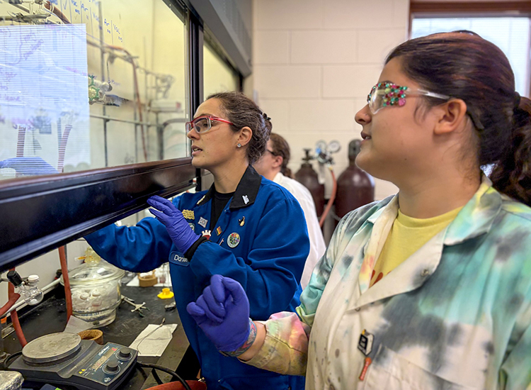 Professor and two students in a biochemistry lab wearing lab coats and glasses. 