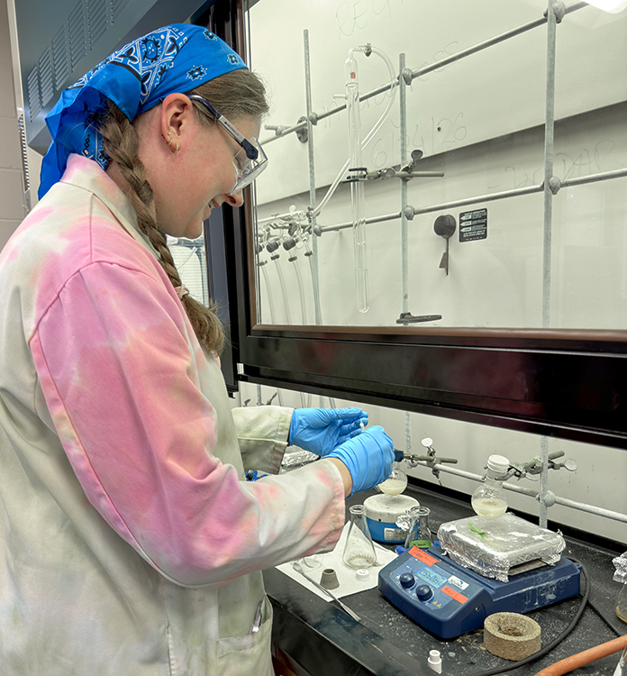 Mallory Gentry in the lab, working under a hood with tools and instruments. 
