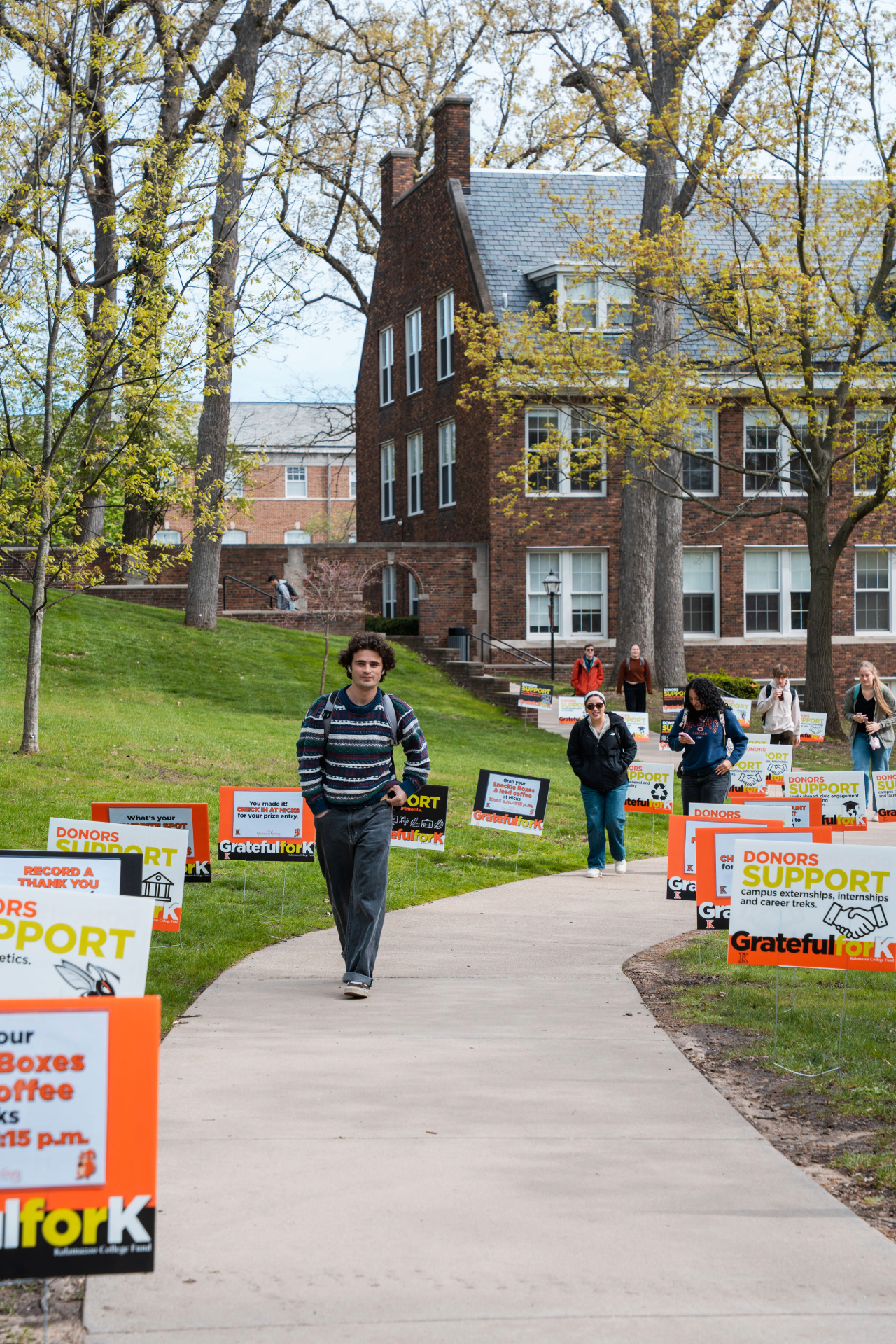 Students walking towards Weimer K. Hicks Student Center with yard signs along the sidewalk. 