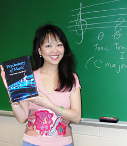 Kalamazoo College Psychology Professor Siu-Lan Tan holds her book in front of a blackboard