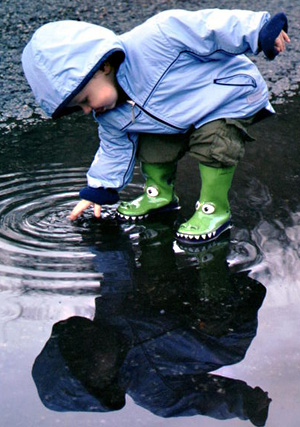 Young boy in rain gear splashes in puddles