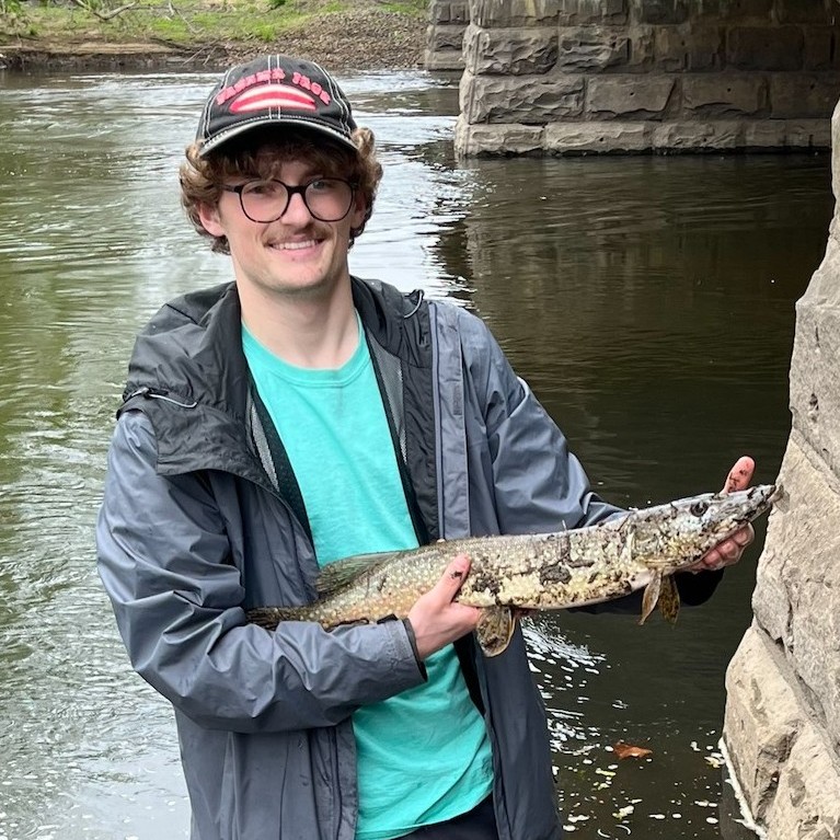Student holding a pike while fishing at a river