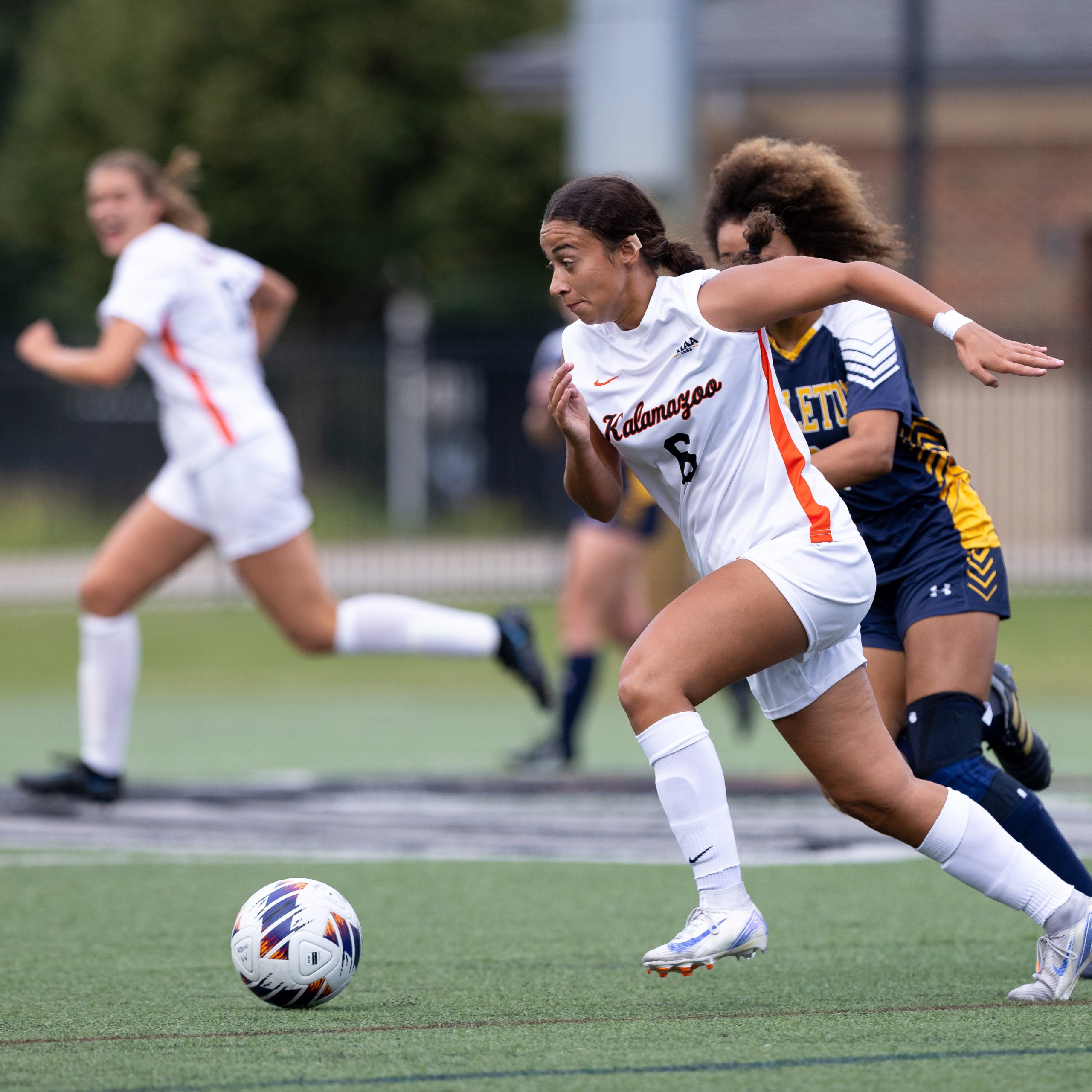 A women's soccer player dribbles down the field
